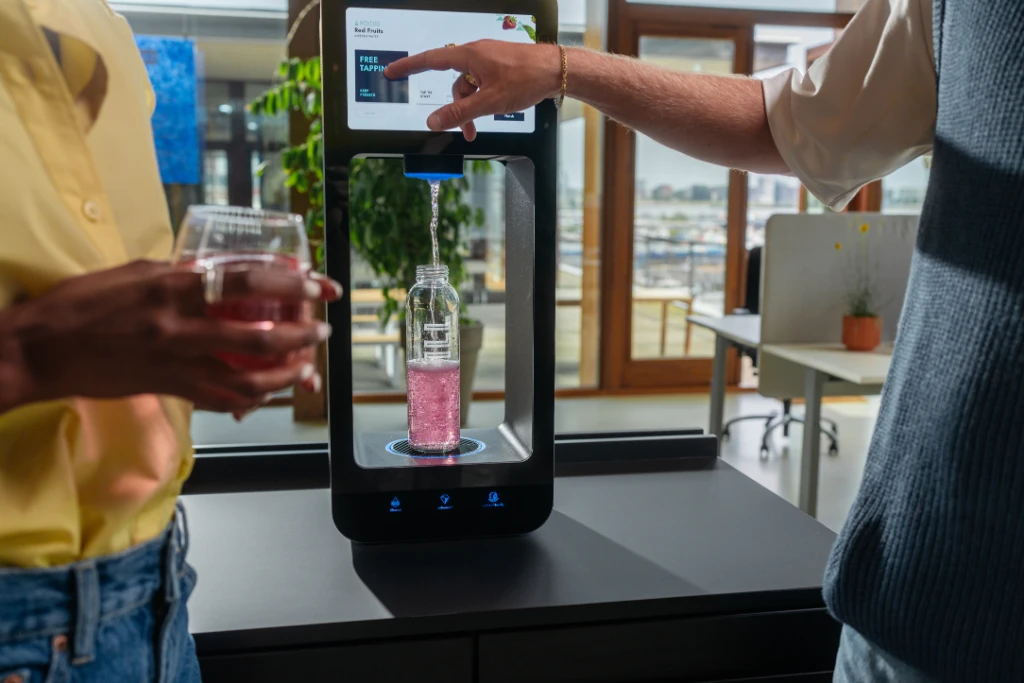 Two people using Aquablu touchscreen water dispenser to fill a bottle with flavoured water